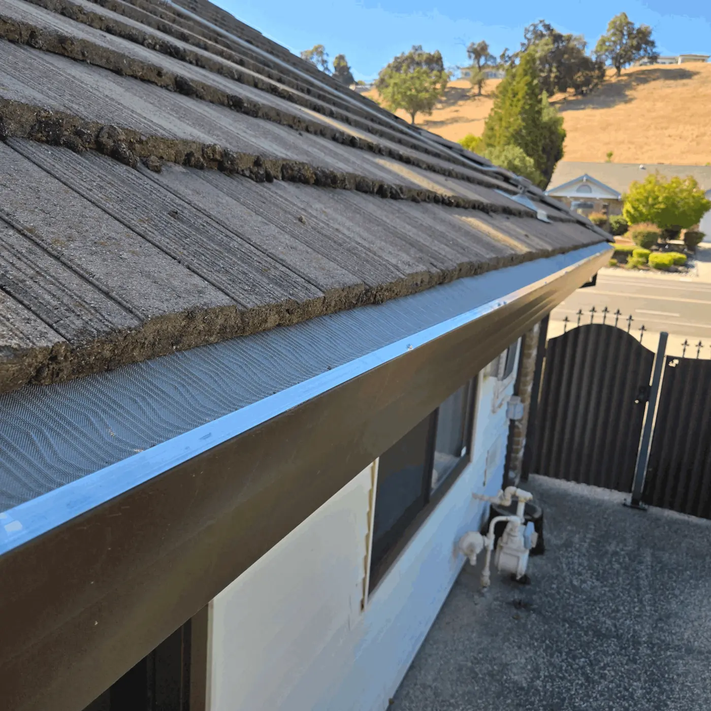 Stainless micro-mesh gutter guard seen from above on a tile-shingle roof