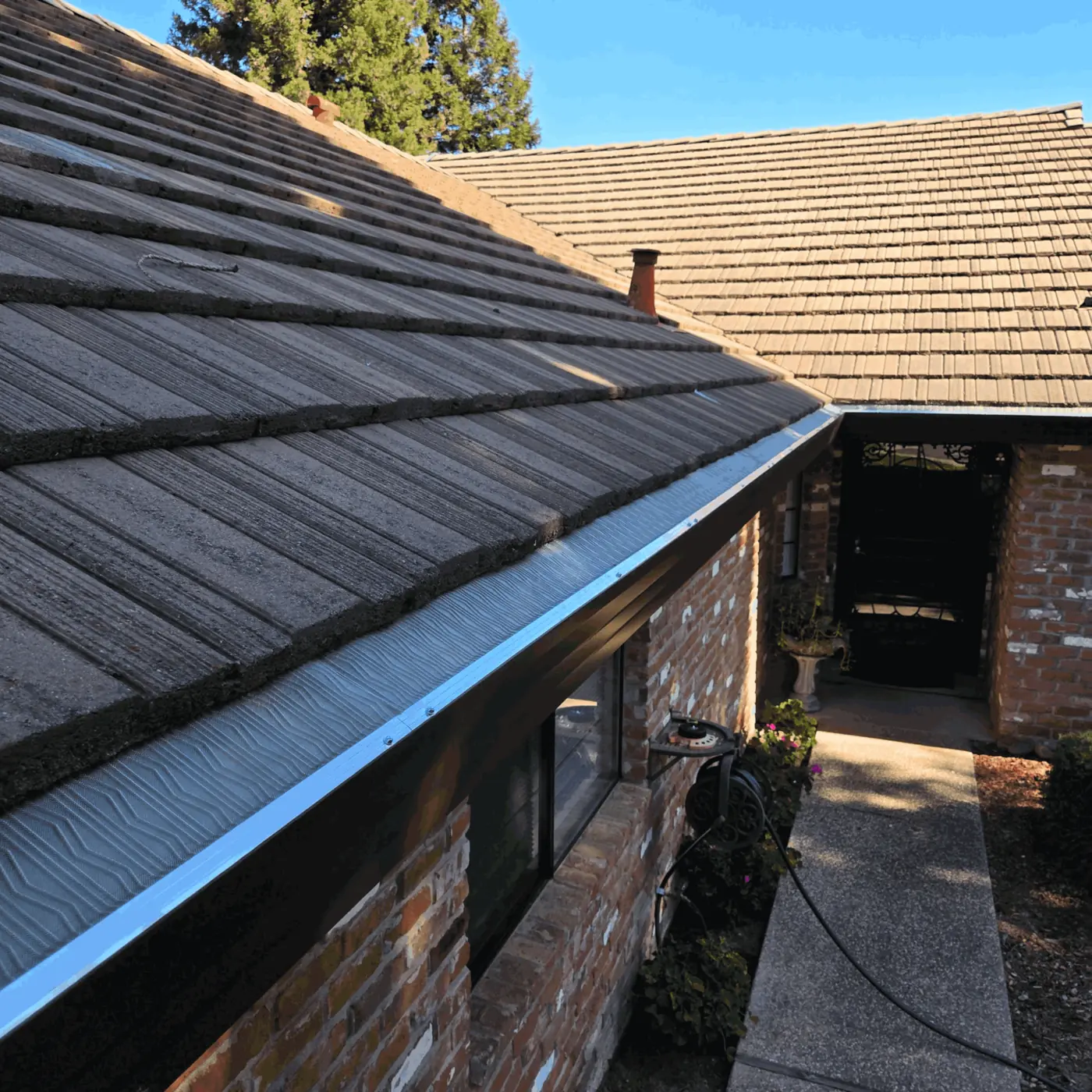 Brown seamless gutter with micro-mesh guard on a brick home with a concrete shake tile roof