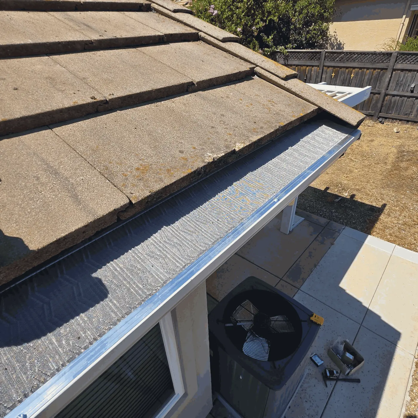 Micro-mesh gutter guard tucked under the first course of a flat concrete tile roof above a backyard patio