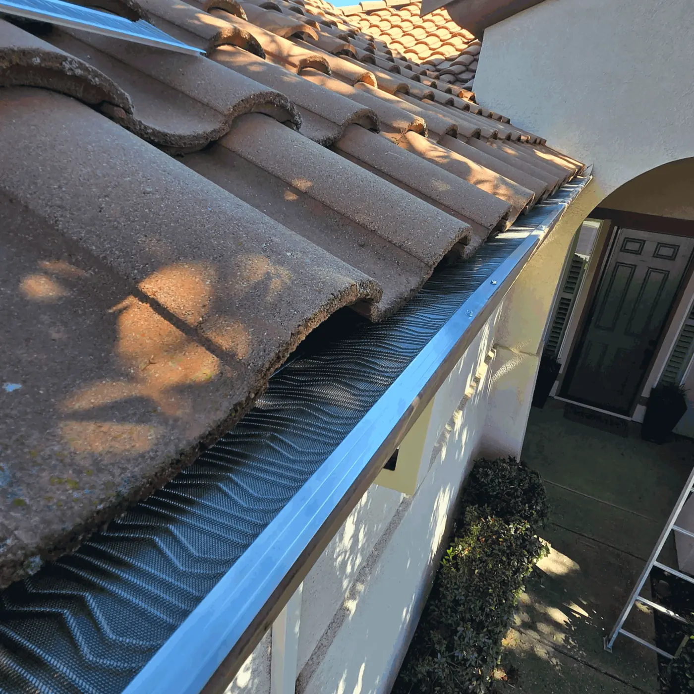 Micro-mesh gutter guard under a Spanish S-tile roof above a stucco arched entry