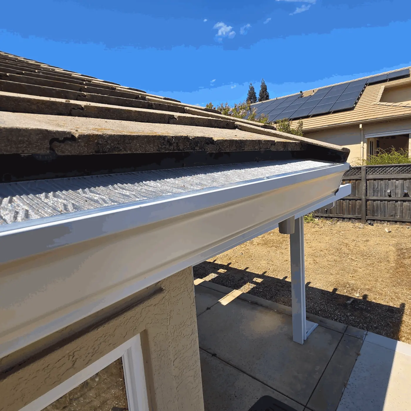 White seamless gutter with micro-mesh guard on a concrete tile roof above a backyard patio cover