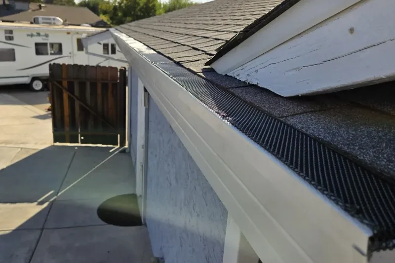 Dark aluminum mesh gutter guard fitted along a white gutter and shingle roof on one of our installs